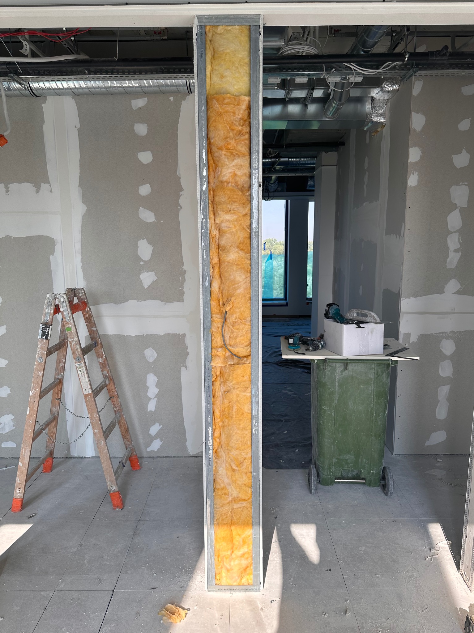 Wnętrze w trakcie prac wykończeniowych: ściany z płyt kartonowo-gipsowych przed szpachlowaniem, ocieplony profil stalowy, drabina, śmietnik z narzędziami w tle.