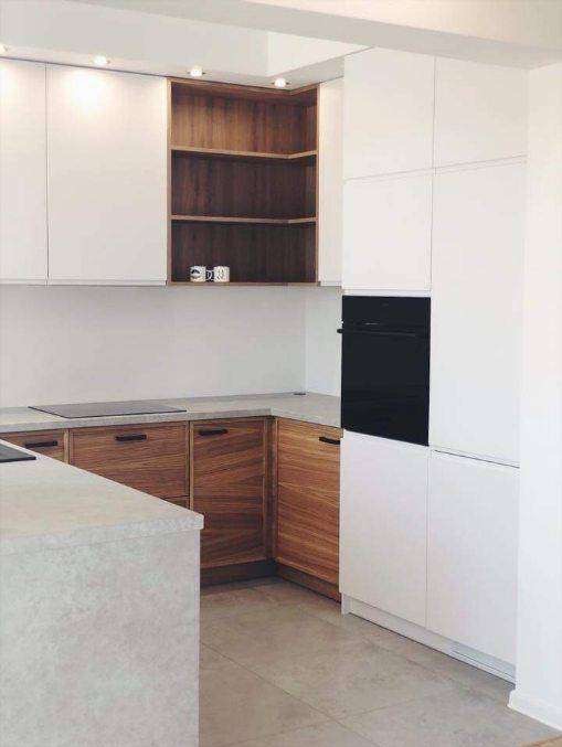 Nowoczesna kuchnia z białymi szafkami górnymi i drewnianymi szafkami dolnymi, z czarnym piekarnikiem w zabudowie i otwartą drewnianą półką narożną z dekoracyjnymi kubkami.