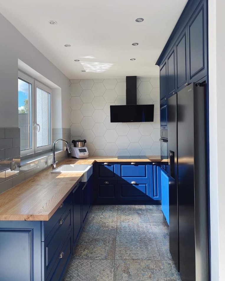 Nowoczesna kuchnia w Gdańsku z granatowymi szafkami, drewnianym blatem i heksagonalnymi płytkami na ścianie, oświetlona punktowymi lampami sufitowymi.