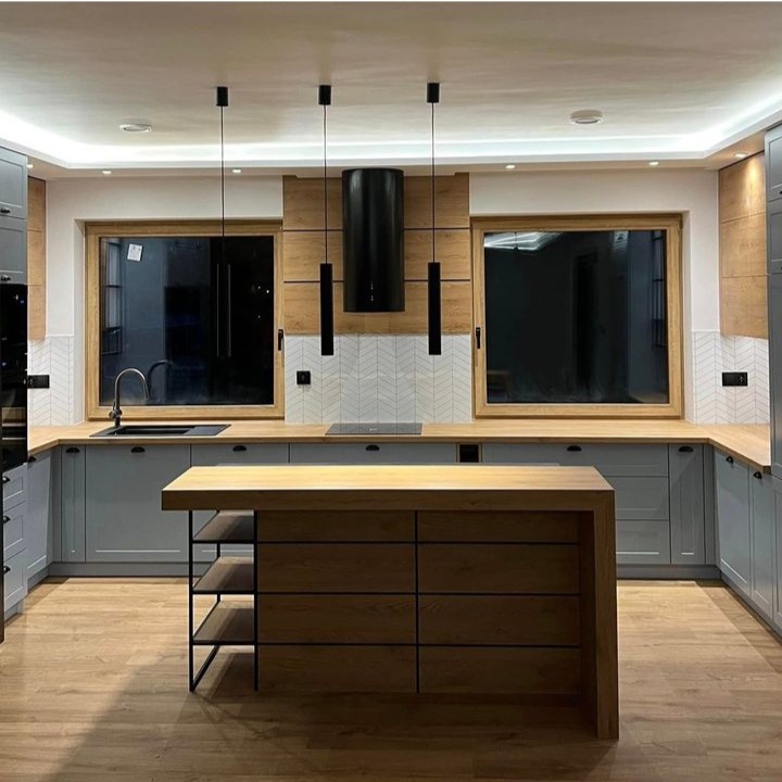 Nowoczesna kuchnia z szarymi szafkami, drewnianym blatem i wyspą z półkami, oświetlona trzema wiszącymi lampami nad wyspą i podświetleniem LED pod sufitem.
