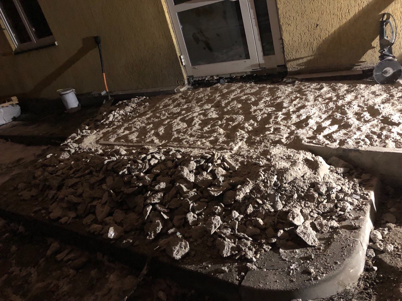 Przygotowanie podłoża pod taras: warstwa gruzu i piasku, widoczna łopata i szlifierka kątowa, prace w toku przy drzwiach balkonowych.