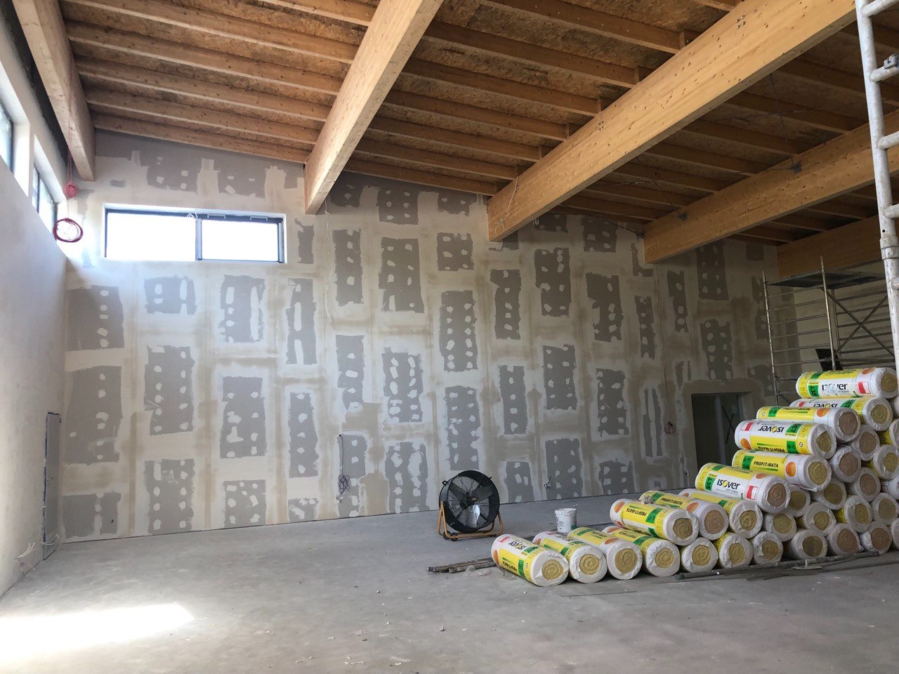 Przygotowanie ścian do gładzi: fragmenty płyt karton-gips na ścianie, szpachlowane połączenia, wentylator, sterta izolacji ISOVER i drewniany strop w surowym wnętrzu.