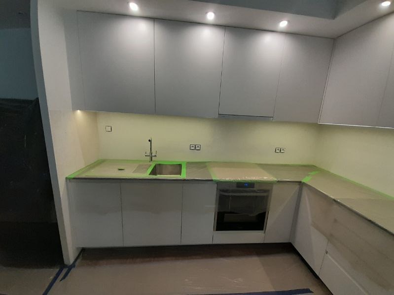 Przygotowanie kuchni do malowania: zabezpieczone folią blaty, zlew i podłoga, widoczne gniazdka elektryczne i nowoczesne, białe szafki kuchenne.