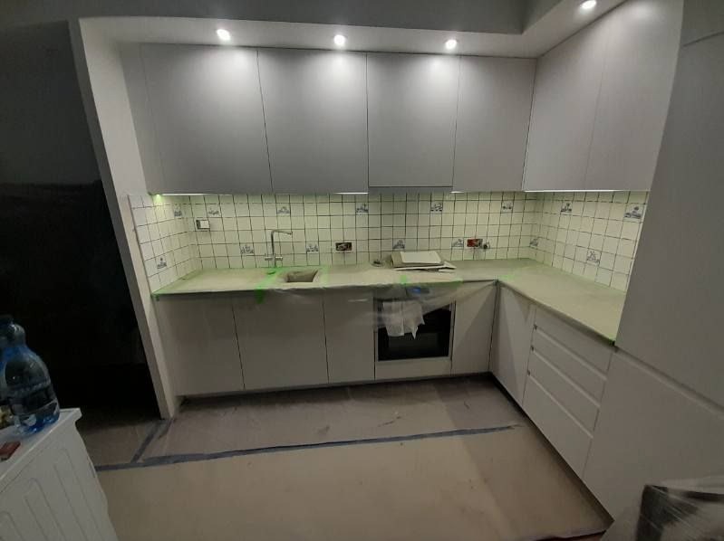 Wnętrze kuchni w trakcie remontu: białe szafki kuchenne zamontowane, blat zabezpieczony folią, widoczne płytki ścienne z dekoracyjnym wzorem oraz zakryty piekarnik.