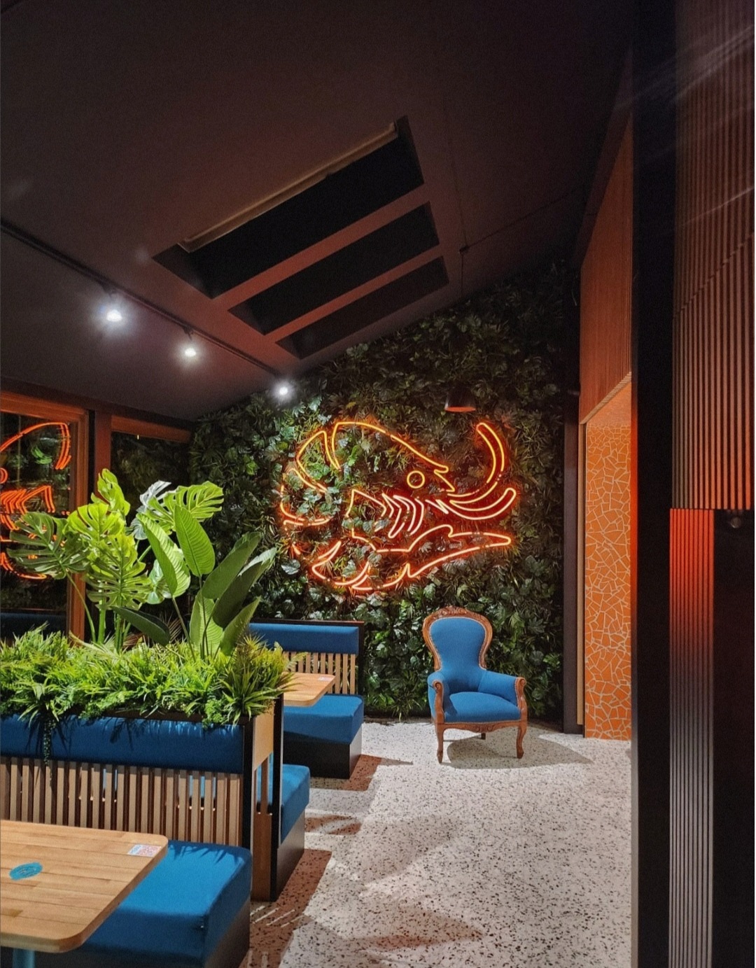 Stylowe wnętrze lokalu z neonem w kształcie słonia na ścianie z roślin, niebieskie kanapy i fotel, mozaika na ścianie, terazzo na podłodze, oświetlenie punktowe.