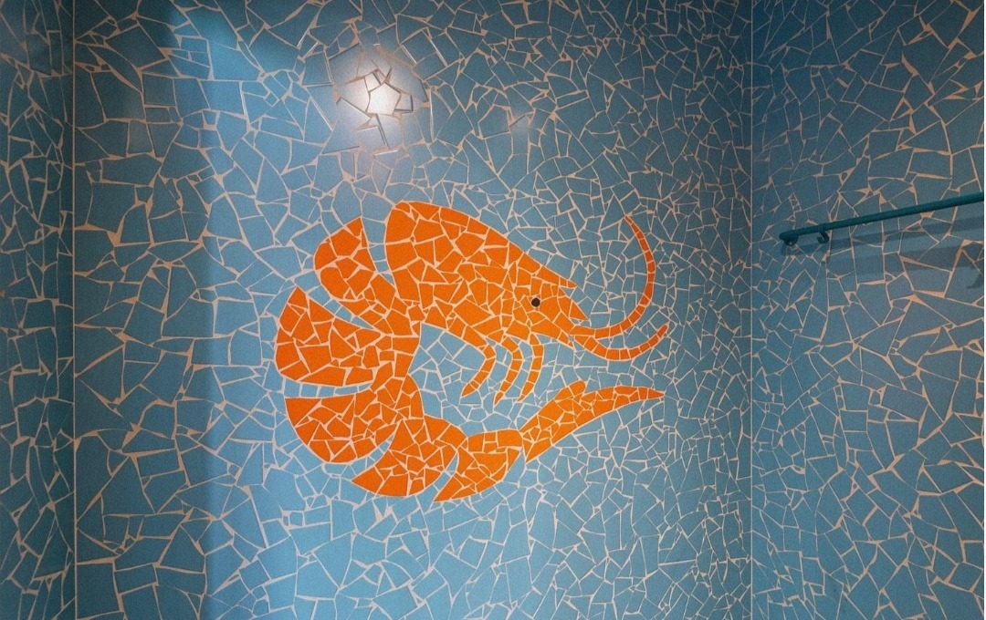 Mozaika ścienna w łazience: błękitne tło z pomarańczowym motywem krewetki. Nietypowe, artystyczne wykończenie wnętrza.