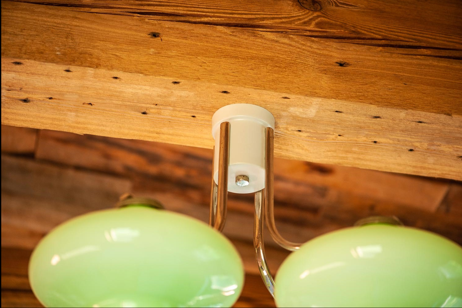 Retro lampa sufitowa z dwoma okrągłymi, zielonymi kloszami, zamontowana na drewnianym suficie z widocznymi śladami po gwoździach.