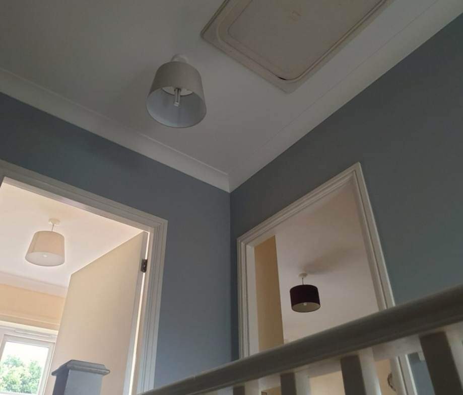 Świeżo pomalowana klatka schodowa w odcieniach szarości i bieli, widoczne detale wykończeniowe, w tle widoczne otwarte drzwi do innych pomieszczeń z oświetleniem.