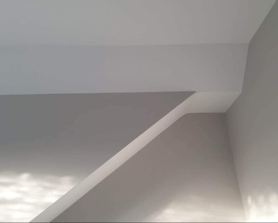 Fragment pomalowanego na szaro pomieszczenia z białym sufitem i listwą sufitową, widoczne załamania ścian i sufitu, delikatne cieniowanie.