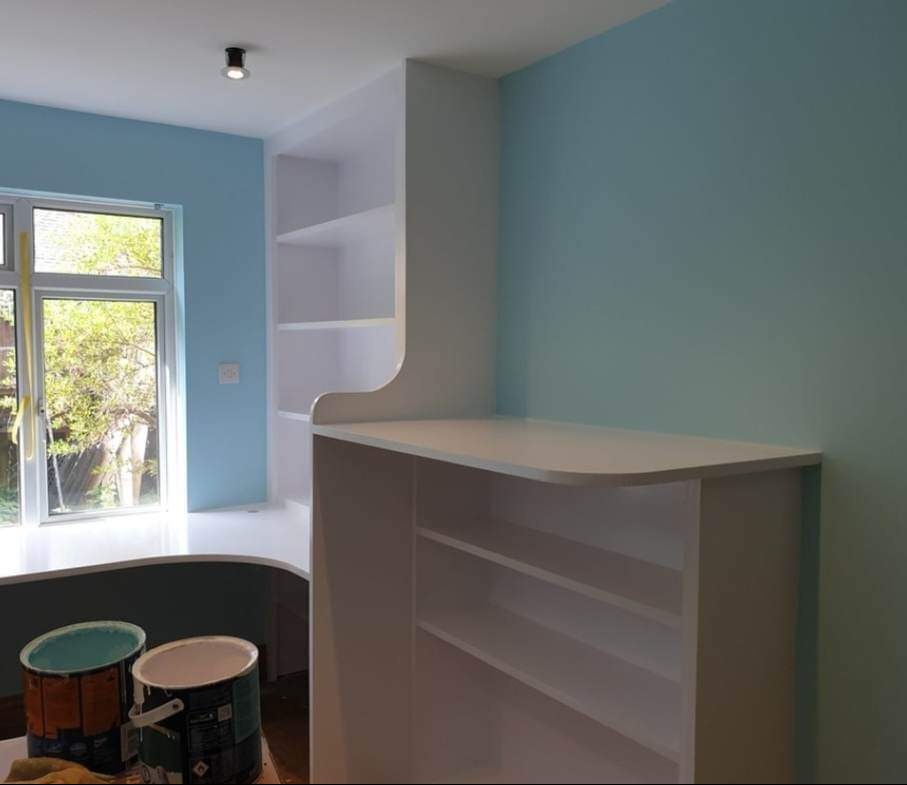 Świeżo pomalowany pokój w odcieniach błękitu z wbudowanym białym regałem, widoczne puszki z farbą w rogu, naturalne światło z okna.