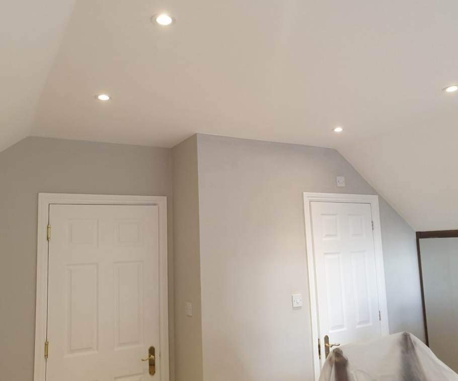 Świeżo pomalowane na szaro wnętrze poddasza w Jeleniej Górze z dwoma białymi drzwiami i oświetleniem punktowym w suficie, zabezpieczone meble folią malarską.