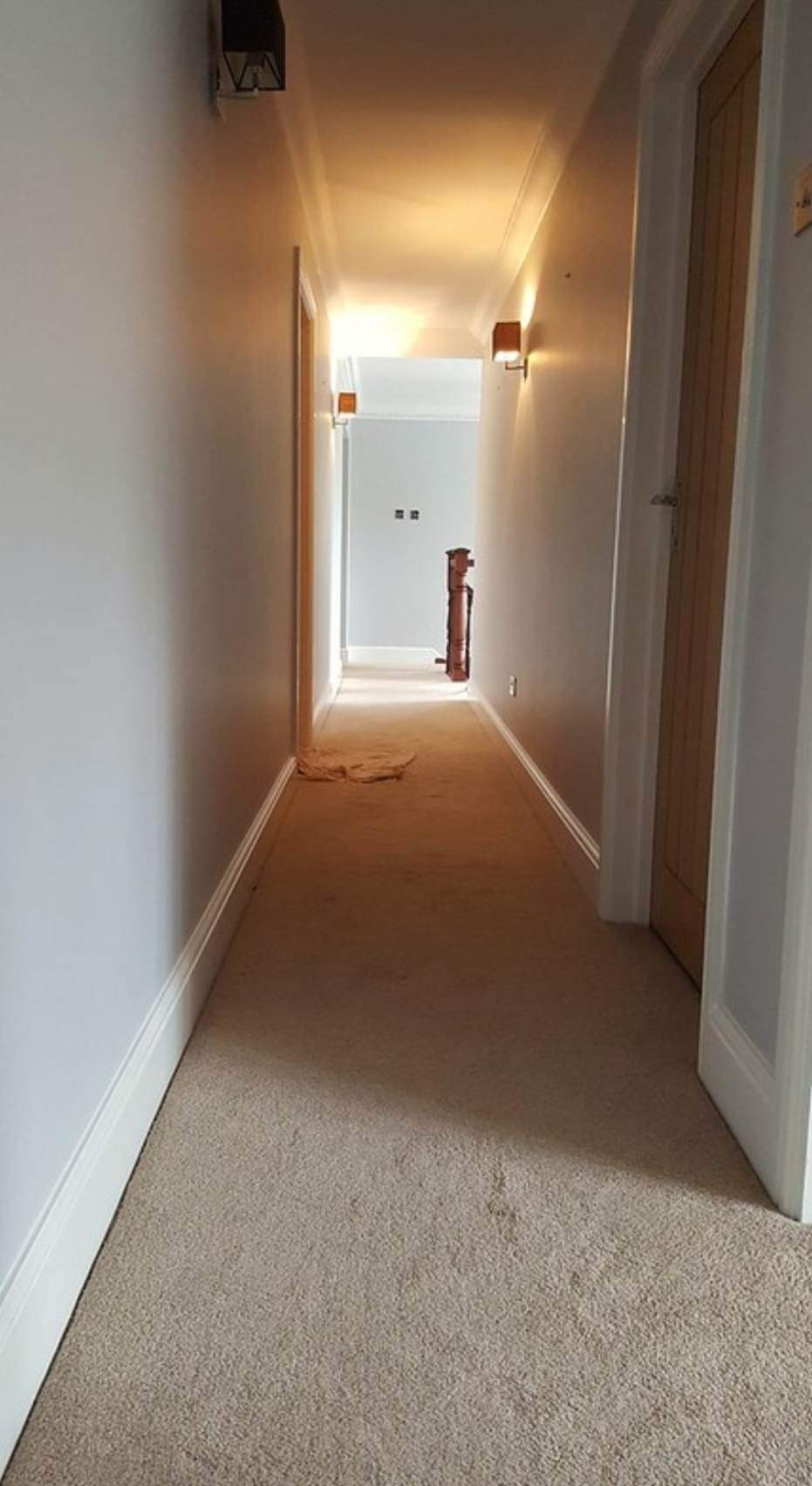 Jasny korytarz po odświeżeniu koloru ścian, widoczny fragment zabezpieczonej podłogi i drewniane drzwi po prawej stronie kadru.