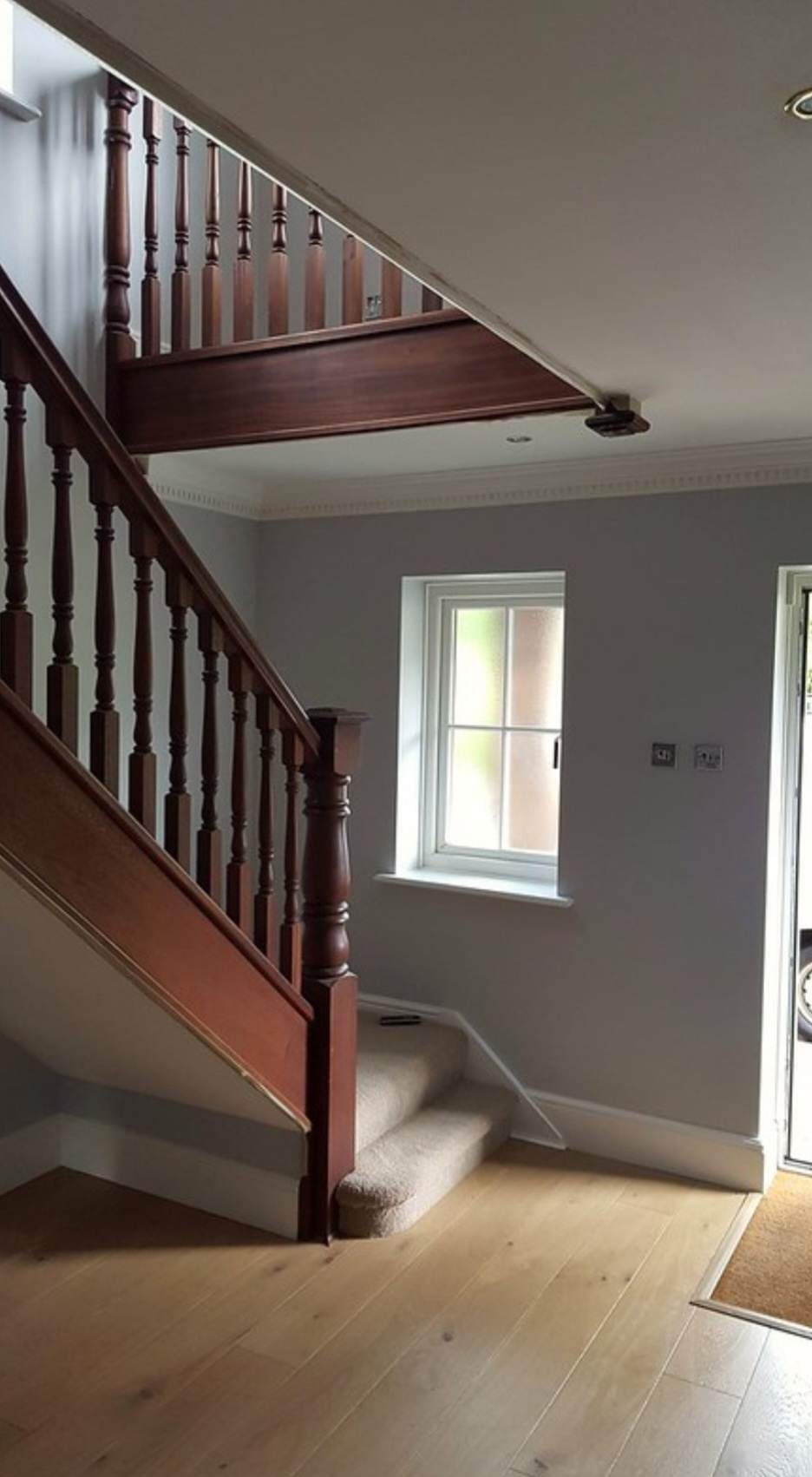 Wnętrze domu z drewnianymi schodami z balustradą, szarymi ścianami, białym oknem i jasną drewnianą podłogą po remoncie.