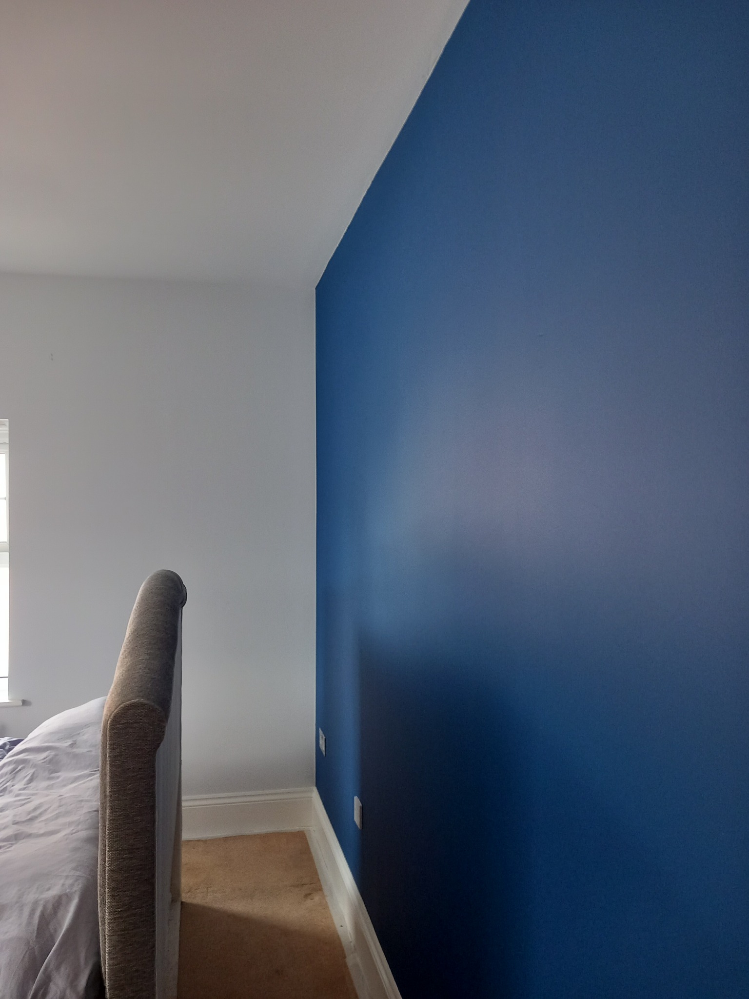 Ściana pomalowana na granatowo w sypialni, widoczny fragment łóżka i biała ściana.  Gładka powierzchnia, świeże malowanie.