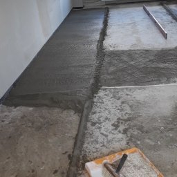 ABCKLASSIK - Wylewka podłogowa w trakcie realizacji, widoczna siatka zbrojeniowa, poziomica i kuweta z pędzlem malarskim.