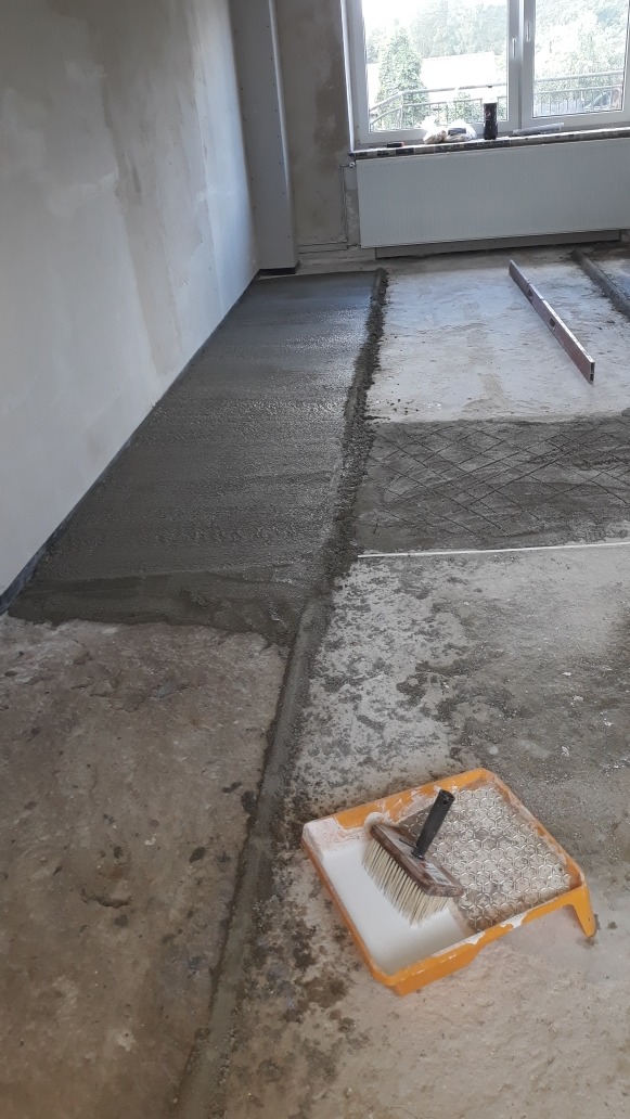 Wylewka podłogowa w trakcie realizacji, widoczna siatka zbrojeniowa, poziomica i kuweta z pędzlem malarskim.