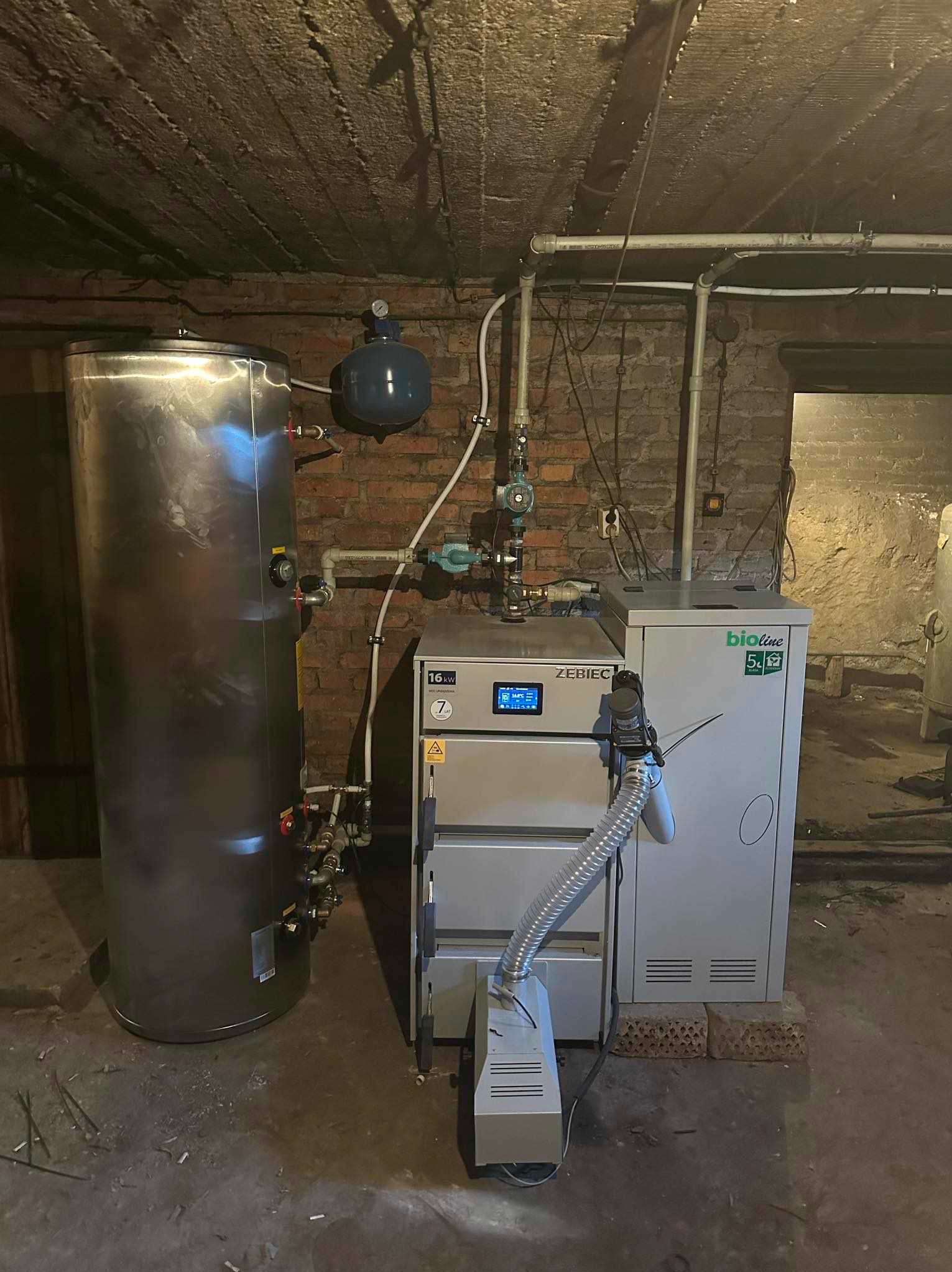 Kotłownia z piecem na paliwo stałe Zebiec i zasobnikiem ciepłej wody użytkowej w piwnicy ze ścianami z cegły.