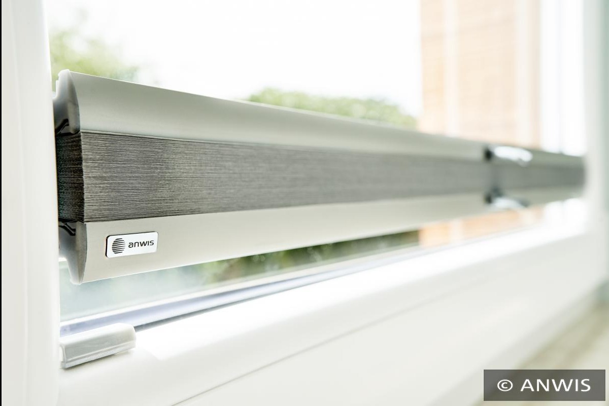 Szara roleta wewnętrzna w kasecie, zamontowana na białym oknie PCV, widoczne logo producenta Anwis.