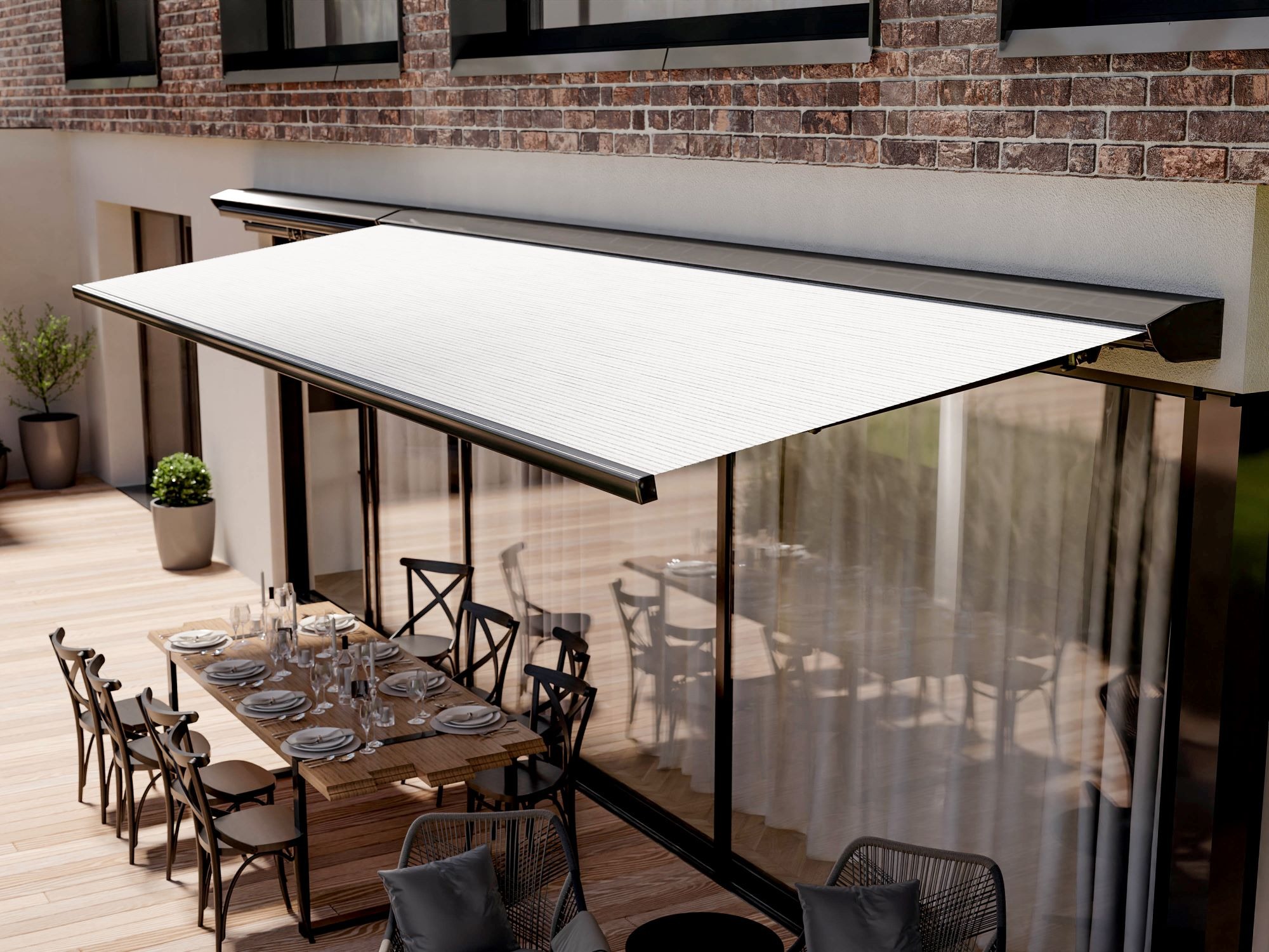 Elegancka, rozłożona markiza w kolorze białym nad tarasem z dużym oknem, na którym widać stół z zastawą dla wielu osób, ceglana ściana budynku w tle.