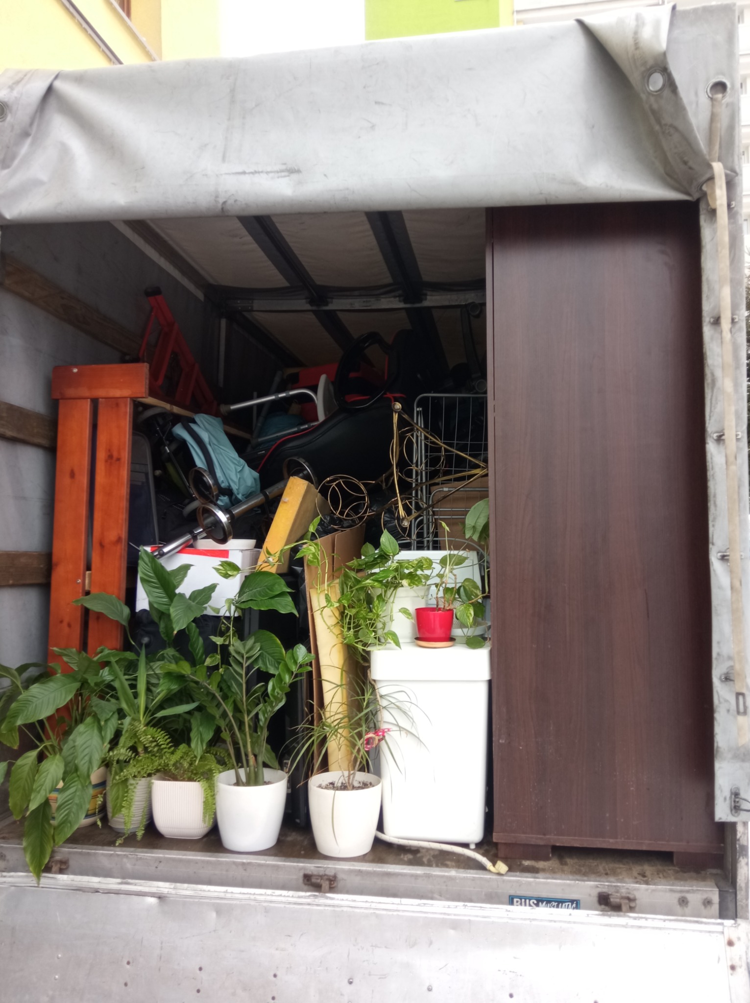 Wnętrze przestrzeni ładunkowej busa wypełnione meblami, sprzętami i roślinami doniczkowymi, widoczne elementy wyposażenia mieszkania zabezpieczone na czas transportu.