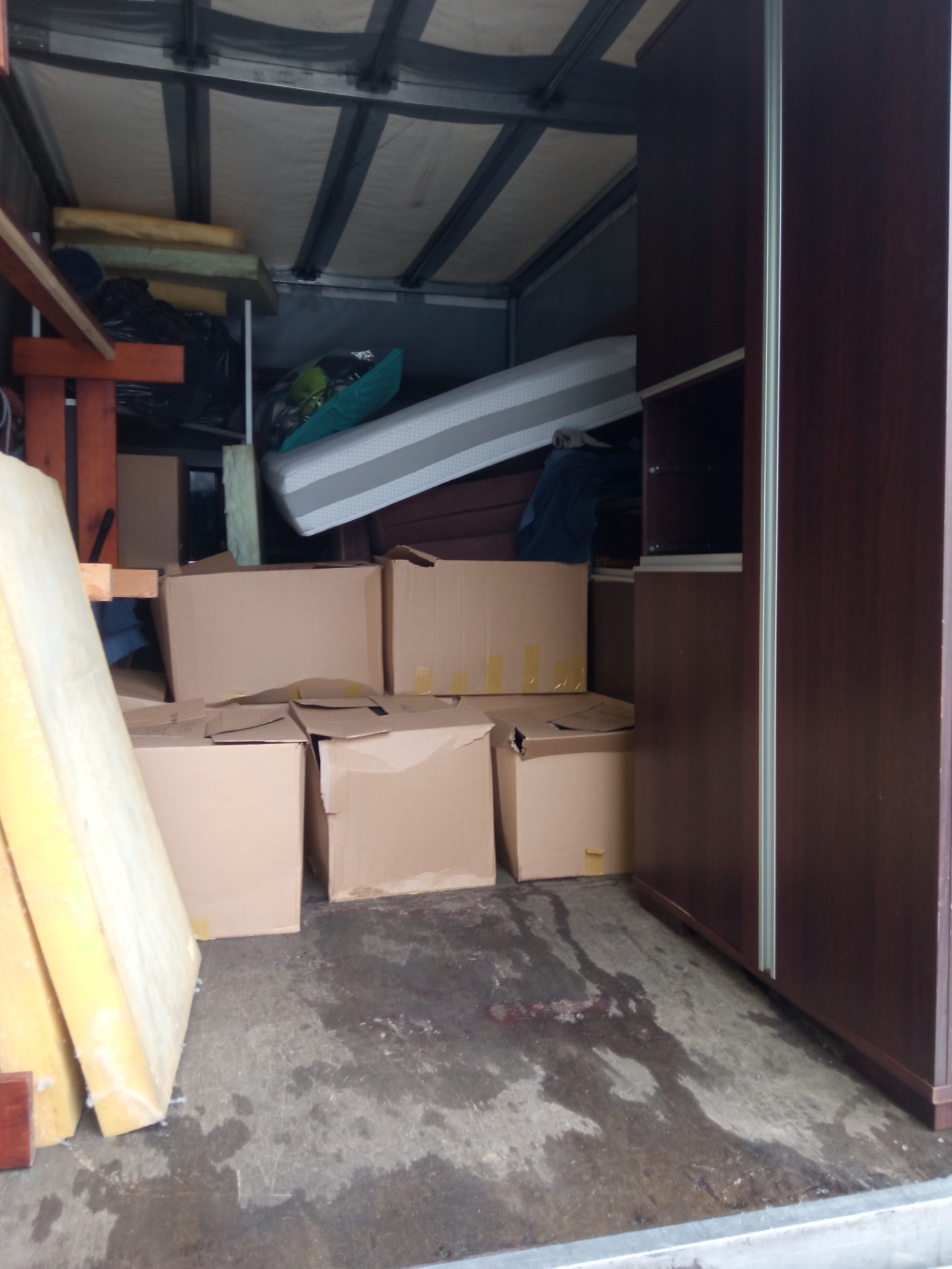 Wnętrze furgonetki załadowanej kartonami, materacem i rozłożoną szafą z przesuwnymi drzwiami podczas transportu, widoczne zabezpieczenia z pianki.