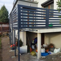 Dominik Gawarecki - Nowoczesna, pozioma balustrada balkonowa z metalu w kolorze grafitowym, zamontowana na betonowym balkonie. Widok z zewnątrz, z widocznymi podporami i otoczeniem.