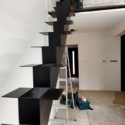 Dominik Gawarecki - Nowoczesne, czarne schody metalowe wspornikowe w trakcie montażu. Widoczna drabina i narzędzia. Minimalistyczny design, surowe wnętrze w trakcie wykończenia.