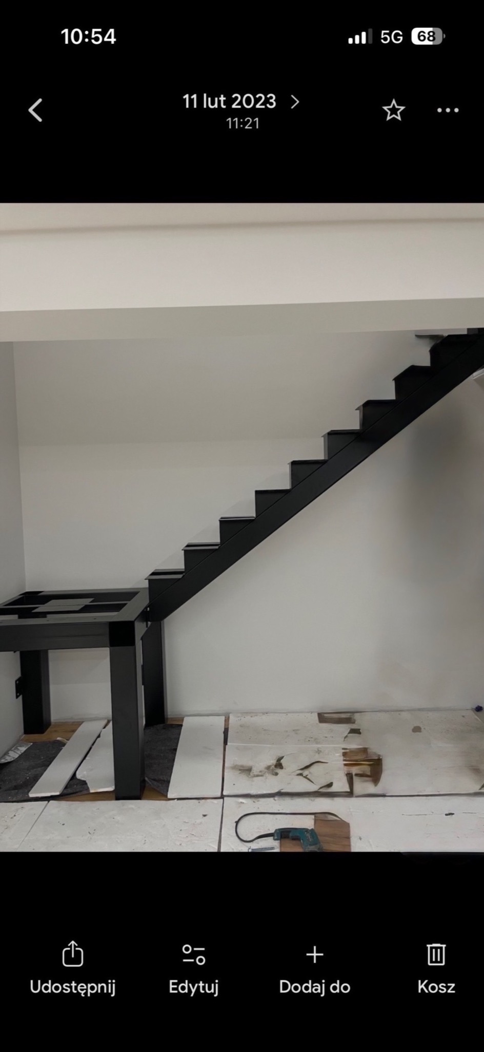 Czarne schody metalowe bez poręczy, z widoczną konstrukcją podestu, w surowym wnętrzu. Na podłodze płyty i narzędzia, co sugeruje etap montażu.