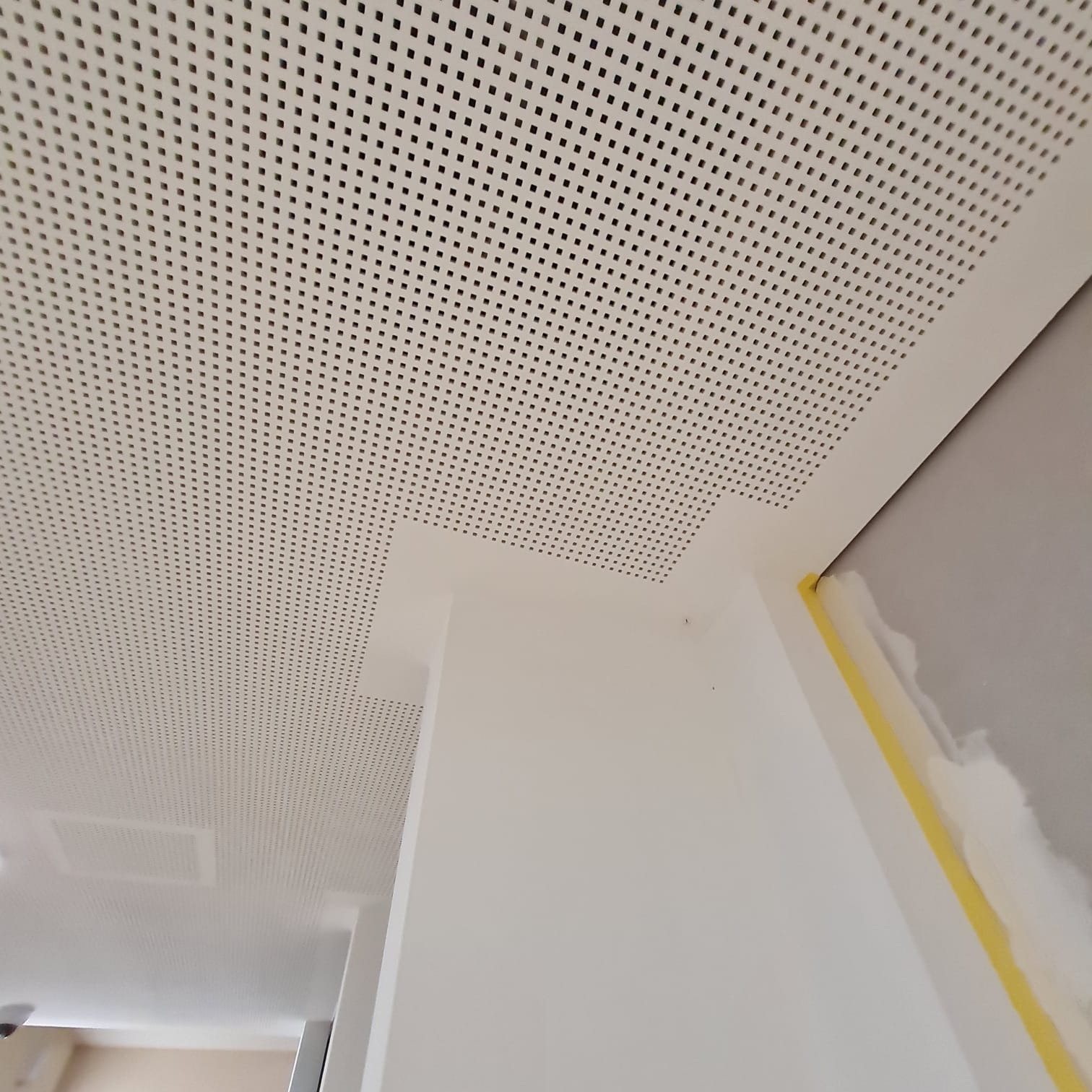 Perforowany sufit podwieszany z płyt kartonowo-gipsowych, widoczne łączenia i taśma malarska zabezpieczająca ściany.