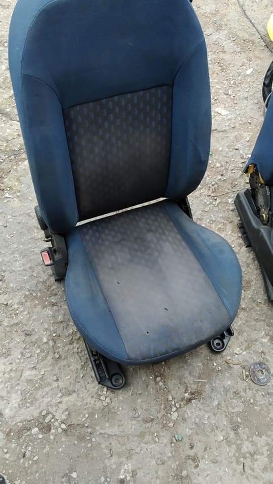 Brudny, niebieski fotel samochodowy z widocznymi plamami i zabrudzeniami na siedzisku, ustawiony na betonowym podłożu.