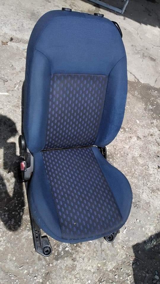 Pojedyncze, niebieskie krzesło samochodowe z ciemniejszym, wzorzystym siedziskiem i oparciem, ustawione na betonowej powierzchni.