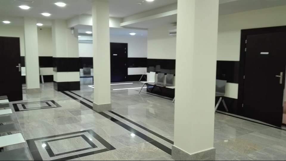 Wnętrze poczekalni z marmurową podłogą w geometryczne wzory, białymi kolumnami i rzędami krzeseł.