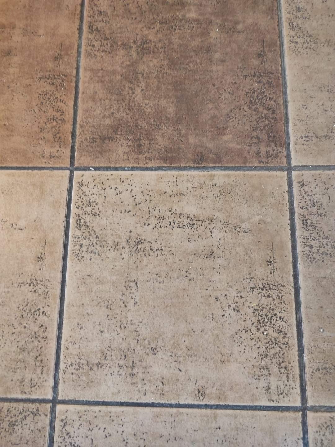 Brudna, beżowo-brązowa kostka brukowa z widocznymi ciemnymi plamami i zabrudzeniami w fugach, widok z góry.