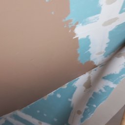 MJ serwis budowlany - Ściana pod skosem w trakcie gładzenia: fragment pomalowany na beżowo, reszta na niebiesko z białymi pasami. Widoczny fragment okna. Praca w toku.