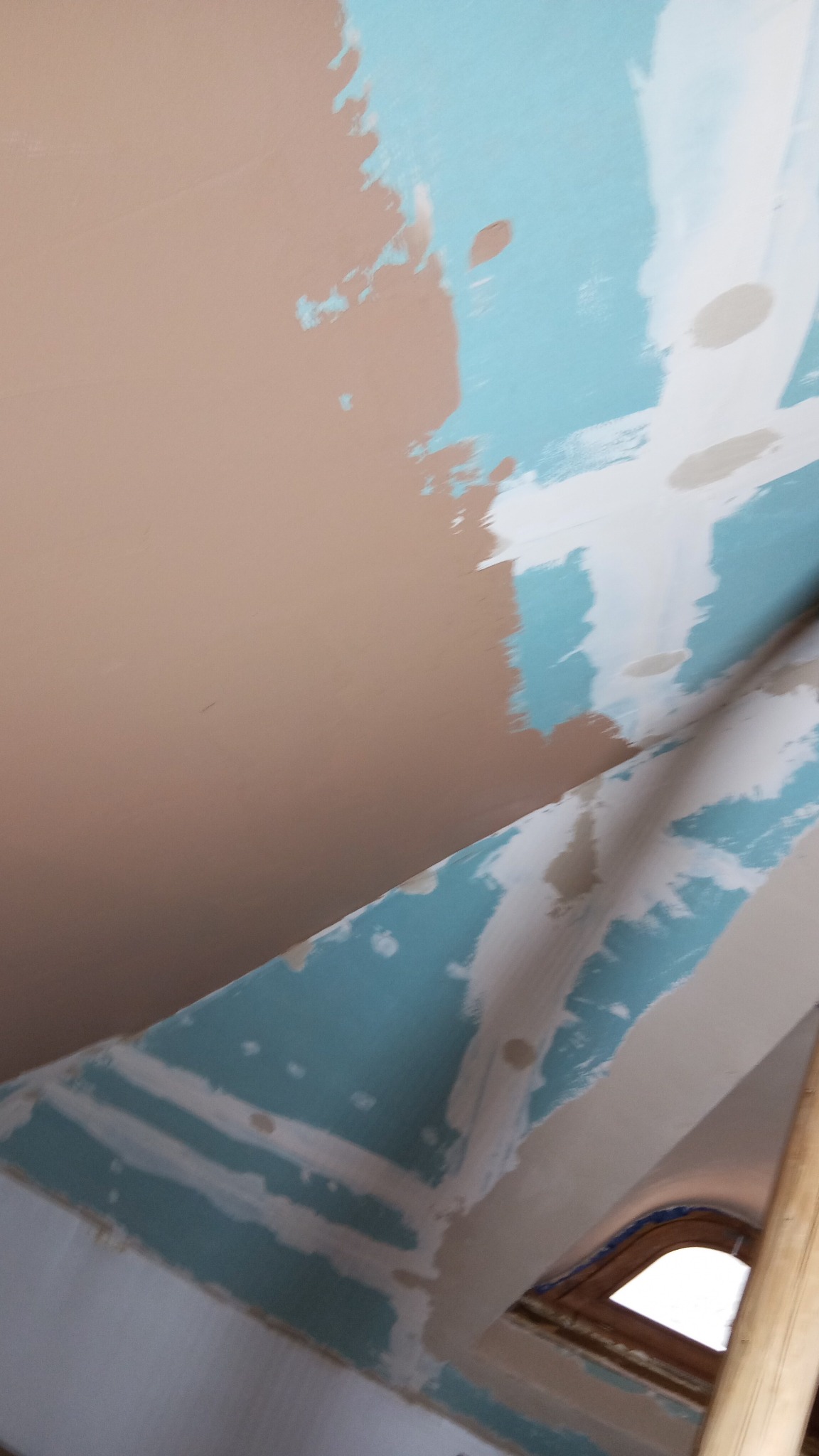 Ściana pod skosem w trakcie gładzenia: fragment pomalowany na beżowo, reszta na niebiesko z białymi pasami. Widoczny fragment okna. Praca w toku.