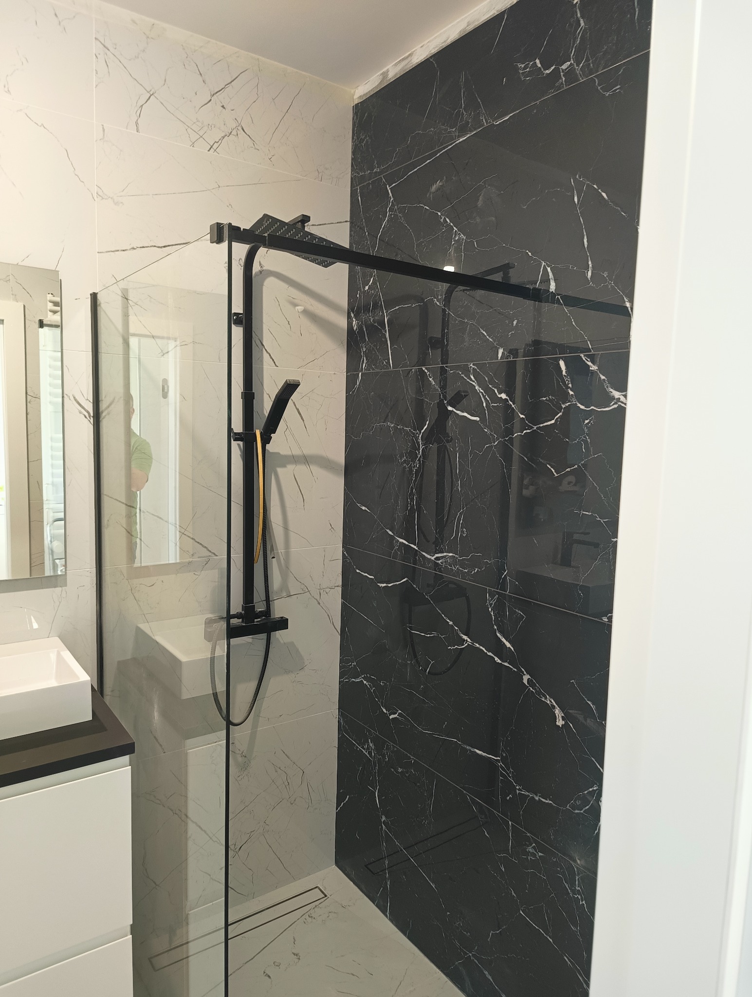 Nowoczesna łazienka z kabiną prysznicową typu walk-in, czarną armaturą i płytkami imitującymi marmur w odcieniach bieli i czerni.