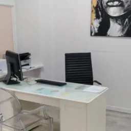 Jasne wnętrze gabinetu z biurkiem z blatem z motywem mapy świata, czarnym krzesłem biurowym i obrazem kobiety na ścianie, logo Biofam w prawym górnym rogu.