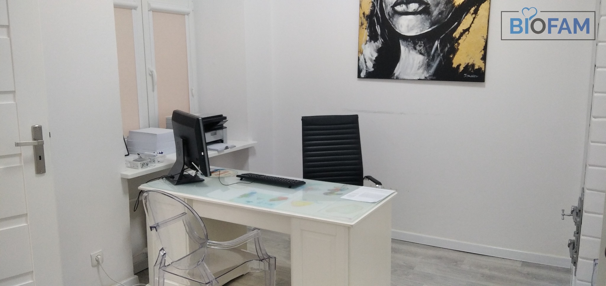 Jasne wnętrze gabinetu z biurkiem z blatem z motywem mapy świata, czarnym krzesłem biurowym i obrazem kobiety na ścianie, logo Biofam w prawym górnym rogu.