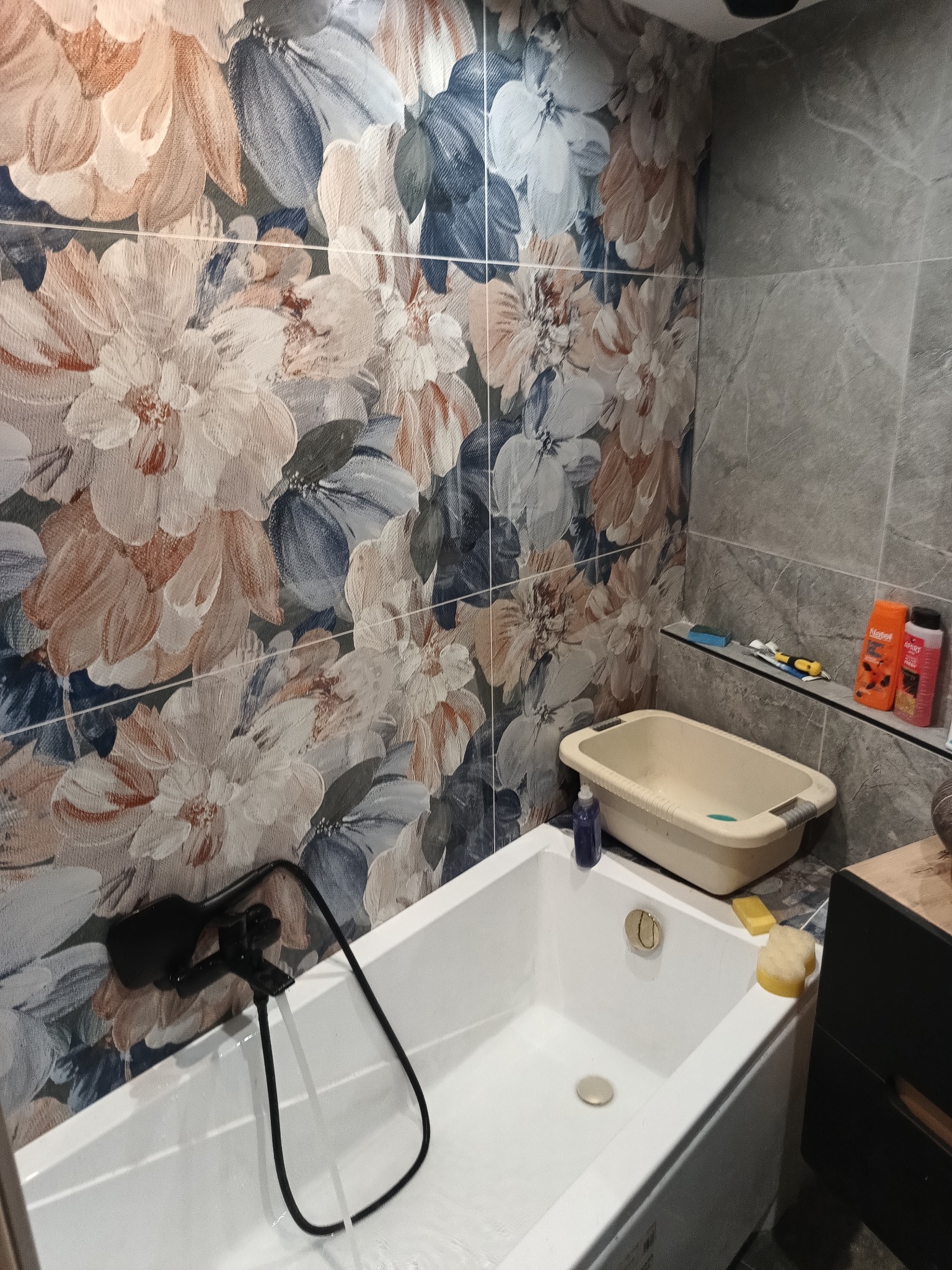 Wykończona łazienka z wanną, czarną armaturą i dekoracyjnymi płytkami w kwiaty na ścianie.