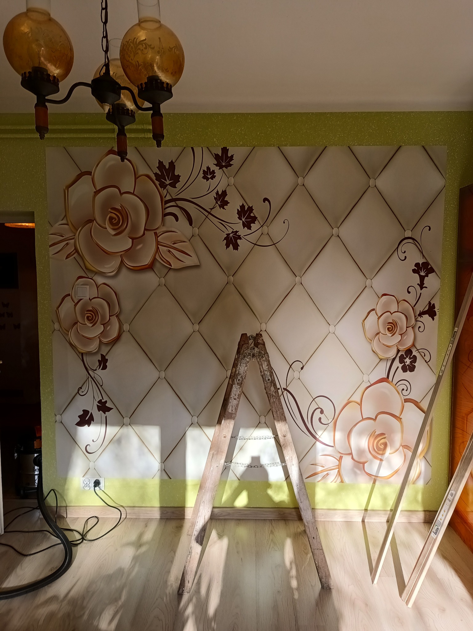 Ściana z tapetą 3D w kwiaty i pikowanym wzorem, drabina malarska oparta o ścianę, widoczny fragment podłogi i wisząca lampa.