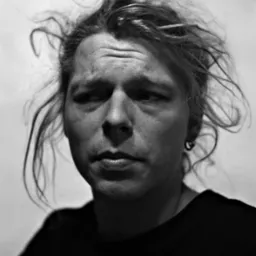 Czarno-biały portret mężczyzny z rozwianymi włosami, patrzącego w bok, z kolczykiem w uchu.