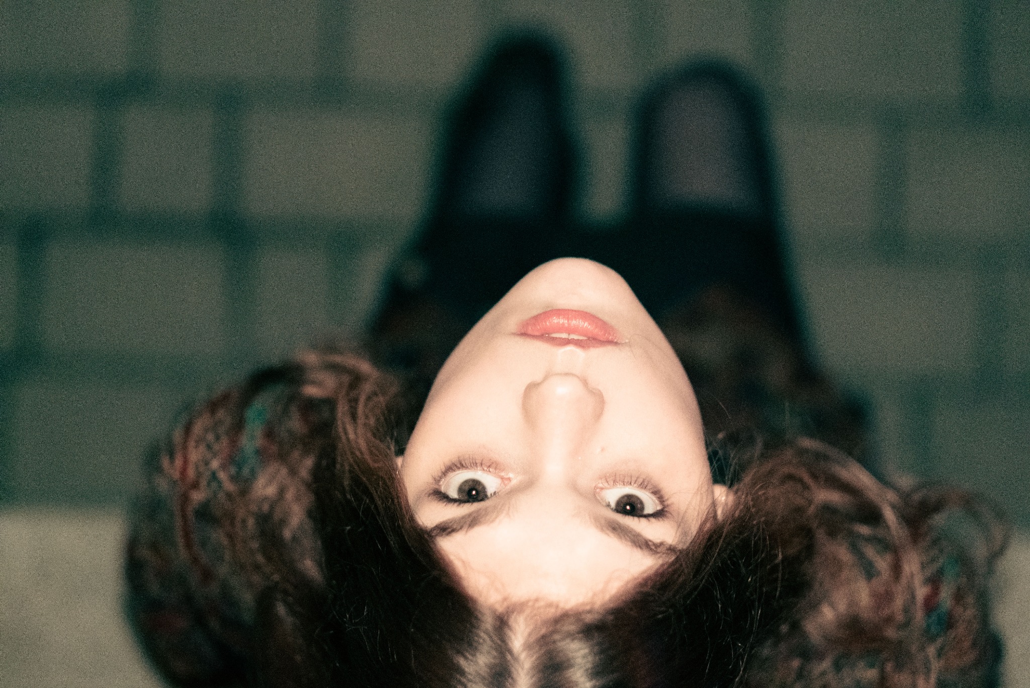 Portret kobiety z szeroko otwartymi oczami, widzianej z góry, z rozmytym tłem przypominającym chodnik.