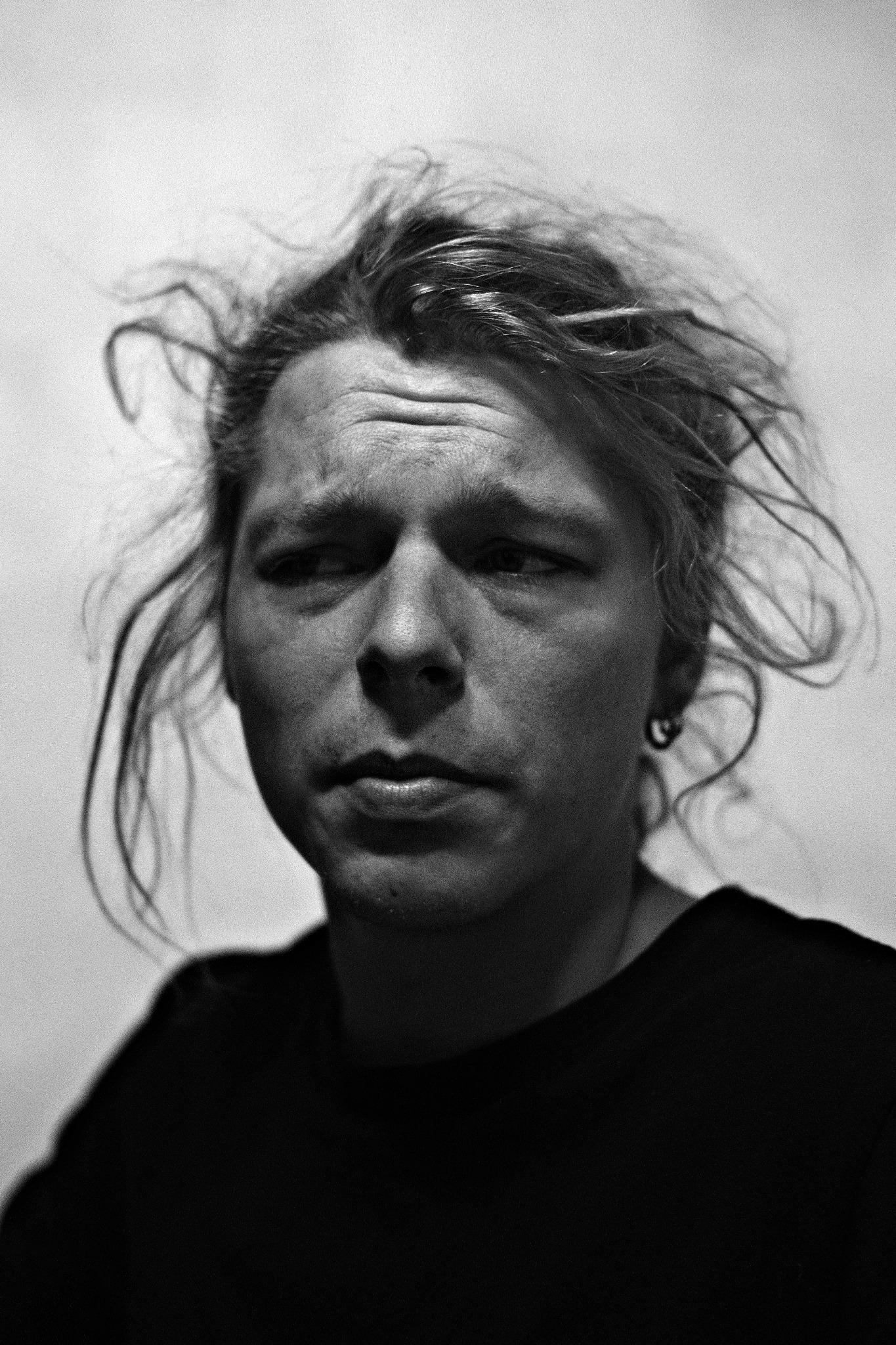 Czarno-biały portret mężczyzny z rozwianymi włosami, patrzącego w bok, z kolczykiem w uchu.