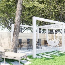 AP DESIGNERS JOANNA BATÓG - Pergola z huśtawką i meblami ogrodowymi na drewnianym podeście, otoczona zielenią i drewnianym płotem, w słoneczny dzień. Widoczne drzewo wkomponowane w konstrukcję.