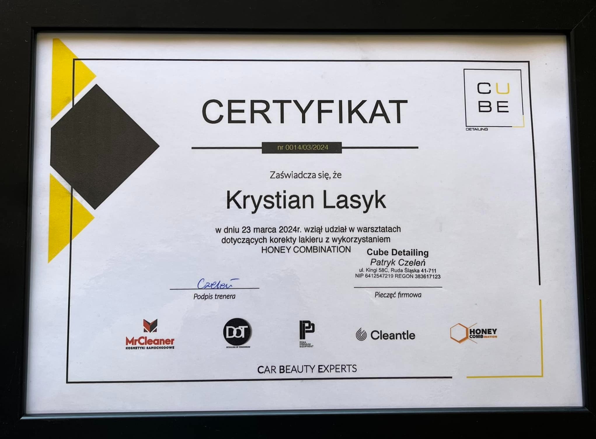 Oprawiony certyfikat ukończenia warsztatów korekty lakieru przez Krystiana Lasyka, wydany przez Cube Detailing, z podpisem trenera Patryka Czelenia, z logotypami MrCleaner, DOT, Poka Premium...