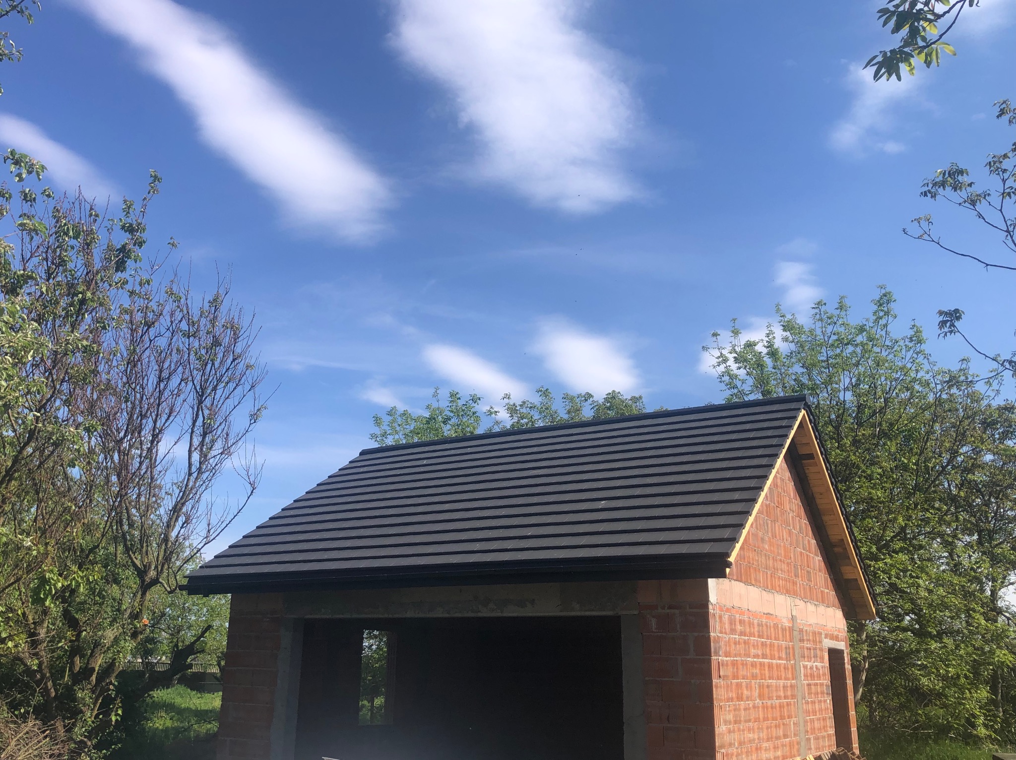 Niedokończony budynek z cegły z nowym, ciemnoszarym dachem, widok z dołu na tle błękitnego nieba z białymi chmurami.