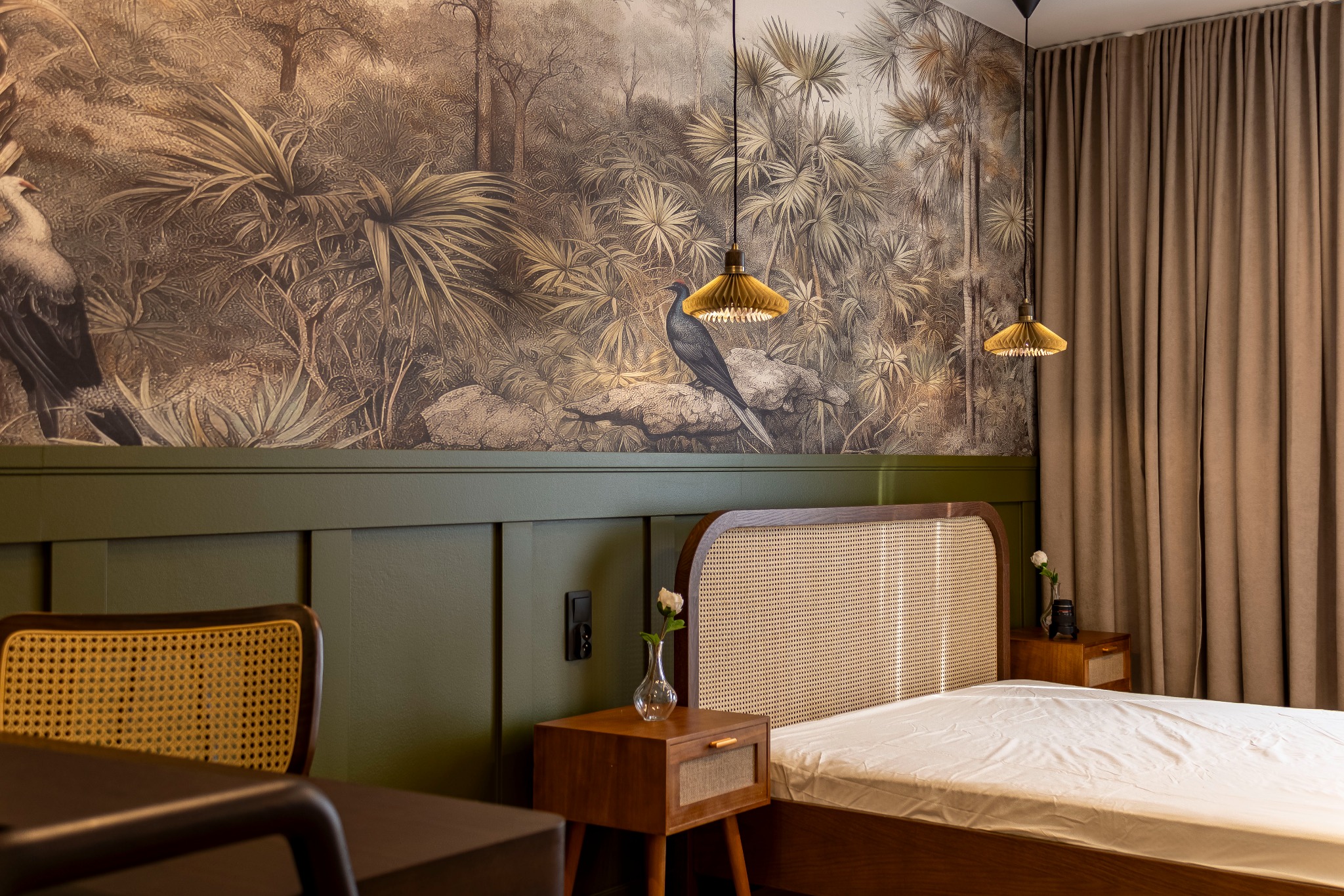 Sypialnia z tapetą w stylu tropikalnym, rattanowym zagłówkiem łóżka i lampkami nocnymi z plisowanymi kloszami.