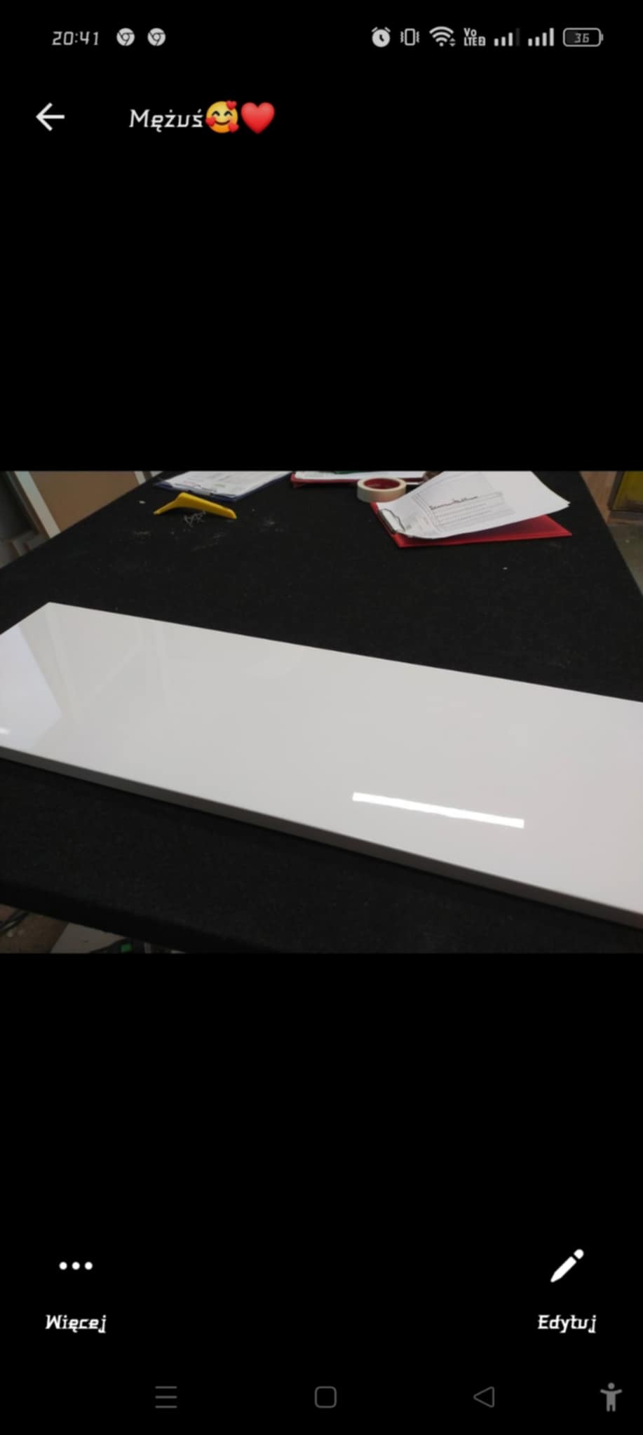 Biały, lakierowany front meblowy leży na czarnym blacie roboczym, widoczne narzędzia i dokumenty w tle.