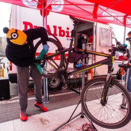 Mobilny Serwis Rowerowy Dr Albin - Mobilny serwis rowerowy: mechanik w czapce Minionka czyści rower na stojaku, w tle bus serwisowy z logo i drugi mechanik.