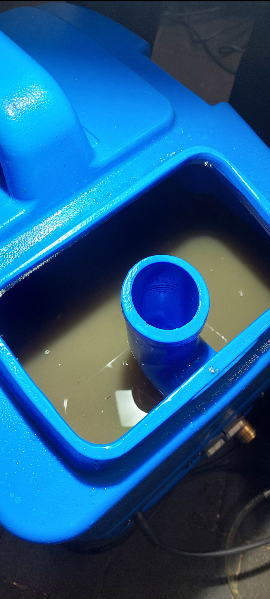 Wnętrze zbiornika na brudną wodę w niebieskim urządzeniu czyszczącym, widoczny wąż odpływowy i osad na dnie zbiornika.